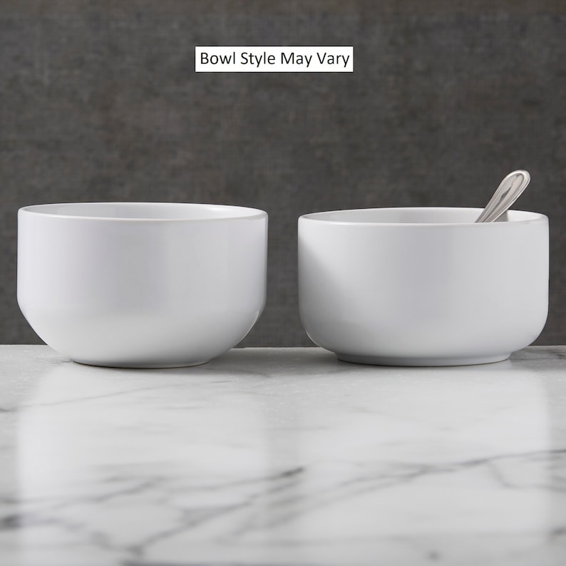 May include: Two white ceramic bowls, one with a spoon inside, on a white marble surface. The text "Bowl Style May Vary" is displayed above the bowls.
