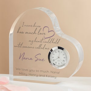 May include: A clear, heart-shaped acrylic clock with a silver clock face. The clock features engraved text in purple and gray, including the name "Nana Sue" and a loving message. A thoughtful gift.