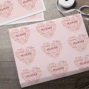 Puede incluir: Papel de regalo rosa con un patr&oacute;n repetido de la palabra "Mommy" en rosa, naranja y amarillo. Los nombres Olivia, Michael y Courtney se repiten en todo el patr&oacute;n.