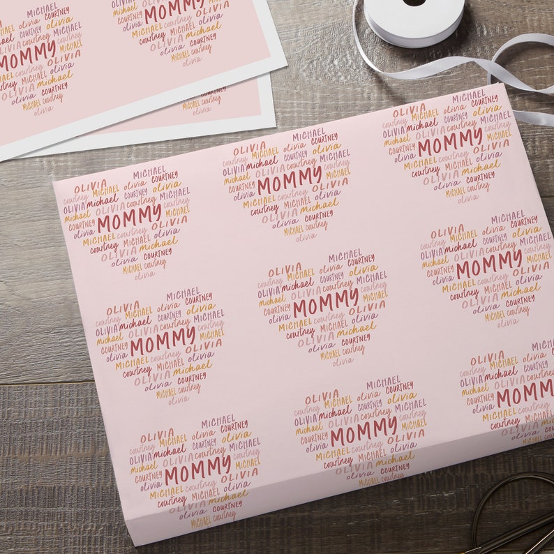 Puede incluir: Papel de regalo rosa con un patr&oacute;n repetido de la palabra "Mommy" en rosa, naranja y amarillo. Los nombres Olivia, Michael y Courtney se repiten en todo el patr&oacute;n.