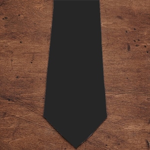 May include: A plain black tie, presented on a wooden background. The tie has a traditional shape with a pointed end and a smooth texture. The dark colour makes it a versatile accessory for different outfits.