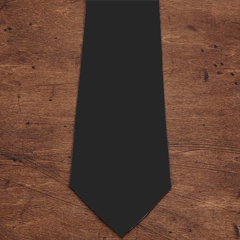 May include: A plain black tie, presented on a wooden background. The tie has a traditional shape with a pointed end and a smooth texture. The dark colour makes it a versatile accessory for different outfits.