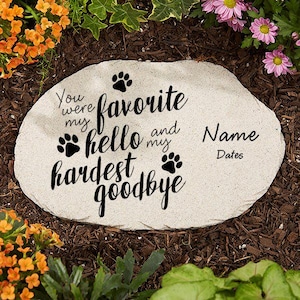 May include: A light-colored stone garden marker with the words "You were my favorite hello and my hardest goodbye." Paw prints and space for a name and dates are also included. The stone is surrounded by flowers and mulch.