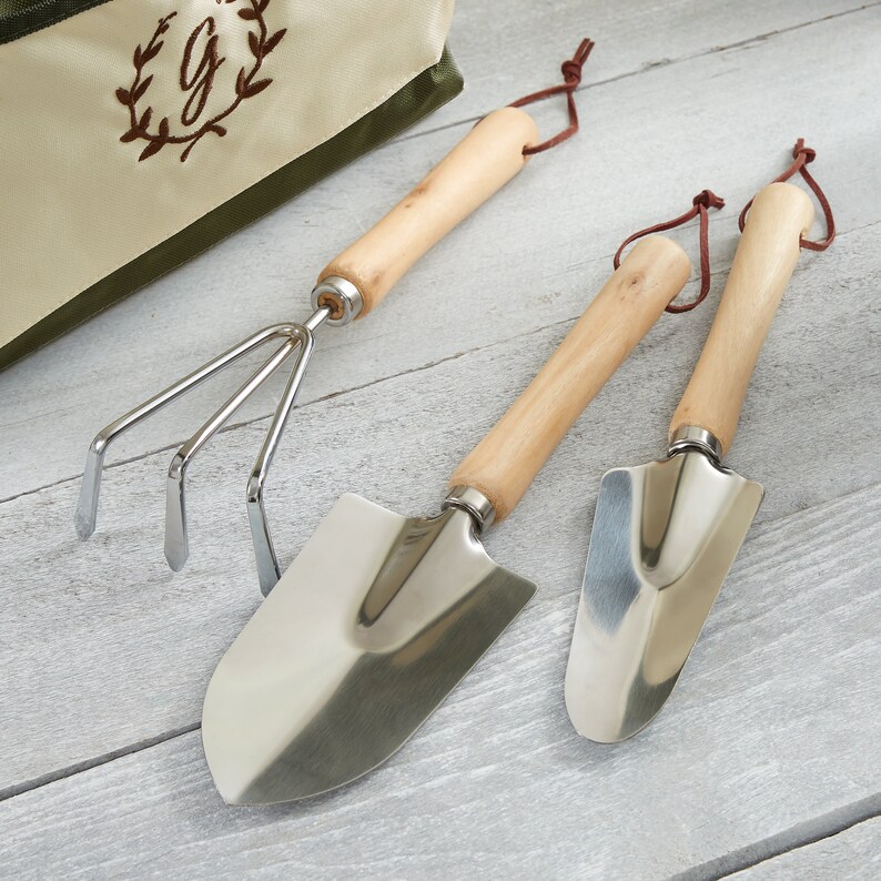 Peut inclure: Trois outils de jardinage avec des manches en bois et des t&ecirc;tes en m&eacute;tal argent&eacute;. Les outils comprennent une truelle, un cultivateur et un r&acirc;teau &agrave; main.