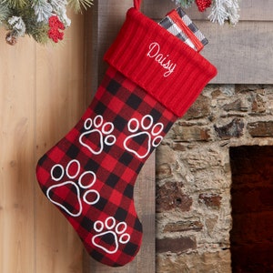 May include: Red and black buffalo plaid Christmas stocking with white paw prints and the name "Daisy" embroidered on the cuff.