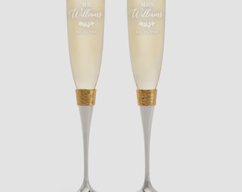 Puede incluir: Dos copas de champán con bandas doradas texturizadas y tallos plateados. Una copa dice "MR. Williams" y la otra "MRS. Williams" con una fecha debajo. Las copas están llenas de un líquido dorado.
