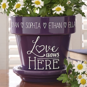 May include: Purple ceramic flower pot with white lettering that reads "Love Grows Here" and "Ryan Sophia Ethan Ella".