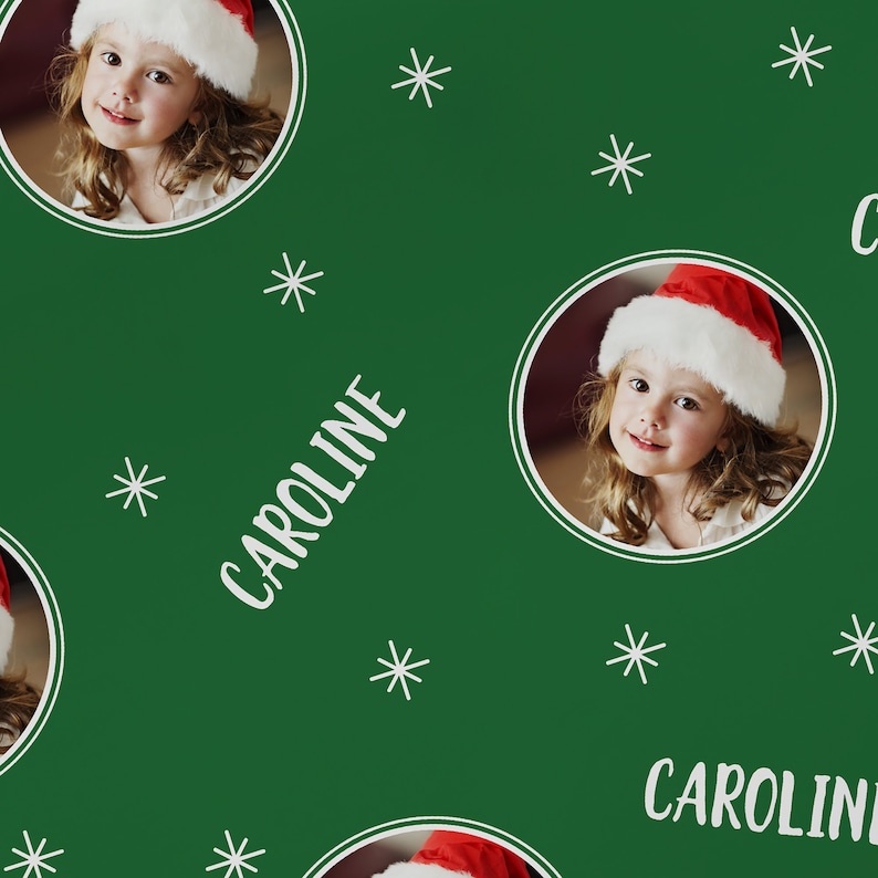 May include: Green wrapping paper with a repeating pattern of white snowflakes, a girl wearing a Santa hat, and the name "CAROLINE" in white text.