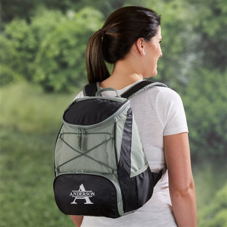 Puede incluir: Una mochila aislante verde y negra con un bolsillo frontal con cremallera y un compartimento grande. La mochila tiene una letra "A" bordada personalizada con el nombre "Anderson" debajo.