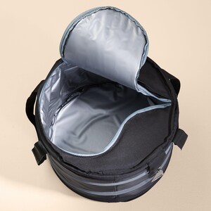 Puede incluir: Una bolsa de enfriador redonda negra con una abertura con cremallera y un forro gris. La bolsa tiene un asa lateral y una correa en la parte superior.
