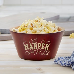 May include: Red wooden popcorn bowl with a gold engraved design of popcorn and the name "HARPER". The bowl is filled with popcorn.