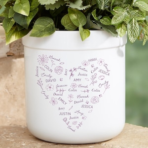 May include: White ceramic planter with a heart-shaped design featuring a variety of names written in purple around the heart. The names include Hannah, Colin, Justin, Amy, David, Jessica, and Emily.