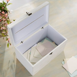 May include: White wooden box with a slot on the top, open to reveal a stack of white envelopes inside. The box has a distressed white finish and a metal latch.
