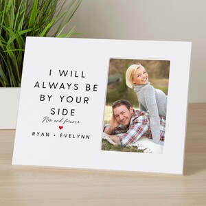 May include: White picture frame with a black inscription that reads "I will always be by your side Now and forever Ryan + Evelynn". A photo of a couple is in the frame.