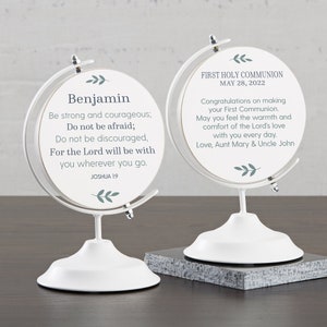 May include: Two white globe-shaped decorative pieces. One features the name "Benjamin" and a Bible verse. The other says "First Holy Communion May 28, 2022" with a message. Both have a white base and a silver metal frame.