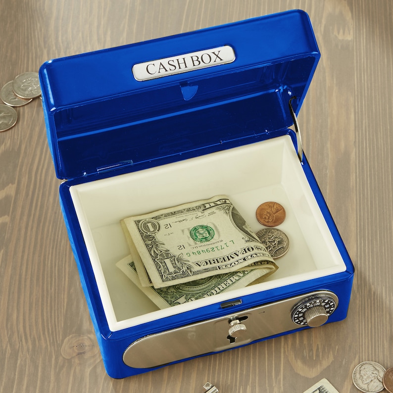 Puede incluir: Una caja de efectivo met&aacute;lica azul con la tapa abierta, revelando un interior blanco. Dentro hay billetes de d&oacute;lar y monedas. La caja tiene una cerradura de combinaci&oacute;n y el texto "CASH BOX" en la tapa.