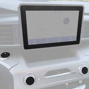 May include: A close-up of a car's dashboard with a carbon fiber trim kit. The kit includes a screen bezel, a knob, and a button. The screen displays the time, temperature, and audio settings. The text on the screen reads "Audio Off", "Phone", "Apps", and "Settings".