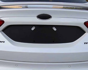 May include: A white car with a black license plate cover. The cover has two holes for license plate screws. The car has a black Ford emblem on the trunk.