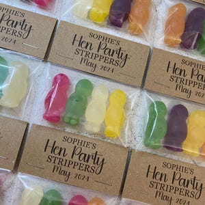 May include: A set of small, clear plastic bags filled with colorful candy shaped like penguins. Each bag has a brown card attached with the text "Sophie's Hen Party Strippers" and a date.
