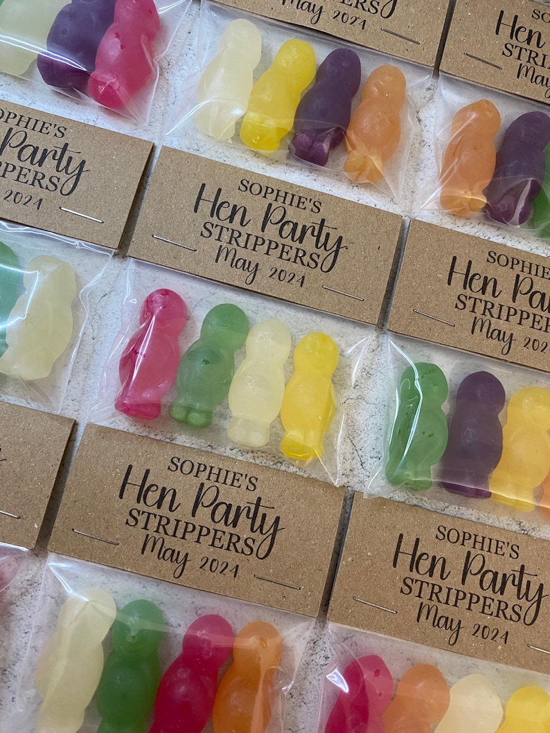 May include: A set of small, clear plastic bags filled with colorful candy shaped like penguins. Each bag has a brown card attached with the text "Sophie's Hen Party Strippers" and a date.