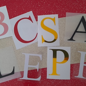 May include: A set of letters, including B, C, S, A, L, E, P, and H, in various colours and styles. The letters are on a white background with a red glitter surface behind them.