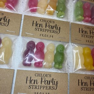 May include: A set of small, clear plastic bags filled with colorful candy. Each bag has a brown card attached with the text "CHLOE'S Hen Party Strippers" and a date.
