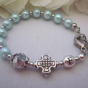 May include: A light blue beaded bracelet with a silver charm in the shape of a cross and a silver bead with the letter "E" on it.