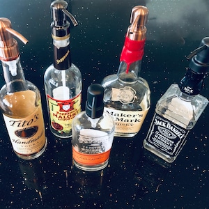 May include: Five different bottles of liquor, including Tito's Handmade Vodka, Maker's Mark Whisky, Jack Daniel's Tennessee Whiskey, and two bottles of liquor with labels that are not fully visible.