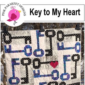 May include: A quilt with a key to my heart design. The quilt is made with a variety of fabrics, including black and white polka dots, blue floral prints, and a white background. The quilt is hanging on a clothesline with two clothespins. The text "Quick Strip Piecing!" is written in white on a red circle in the bottom right corner of the image.
