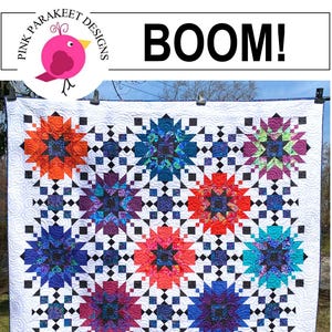 Könnte beinhalten: Ein farbenfroher Quilt mit einem Sternmuster in Orange-, Blau-, Lila- und Rosatönen. Der Quilt hat einen weißen Hintergrund mit schwarzen quadratischen Akzenten. Das Wort "BOOM!" wird oben zusammen mit einem rosa Vogellogo angezeigt.