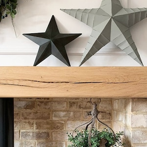 May include: A rustic wooden mantel with a distressed finish, featuring two metal star decorations in gray and black. The mantel is mounted above a brick fireplace.