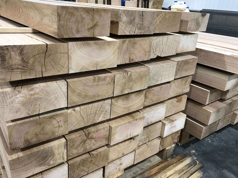 May include: A stack of large, rectangular wooden beams with visible grain patterns. The beams are light brown in color and have a rough, unfinished texture.