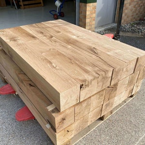 May include: A stack of rough-cut, light brown wooden planks, likely oak, on a pallet. The planks are stacked neatly and have a natural, rustic appearance.