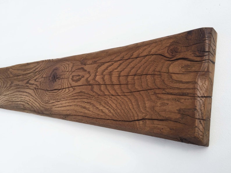 May include: A long, rustic wooden beam with a natural brown finish. The wood has a knot and a grain pattern. The beam is slightly curved.