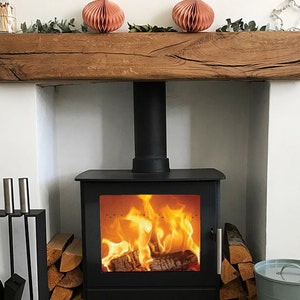 May include: A black wood-burning stove with a roaring fire inside. The stove is set into a white fireplace with a wooden mantel above. The mantel is decorated with two pink paper lanterns and greenery.