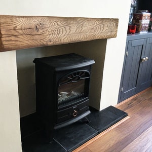 May include: A black electric fireplace with a realistic flame effect sits in a white fireplace surround with a rustic wooden mantel. The fireplace is in a room with dark wood floors and a dark wood cabinet with doors.