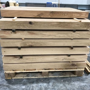May include: A stack of six wooden planks on a pallet. The planks are light brown and have a rough texture. The pallet is made of wood and has a brown stain.