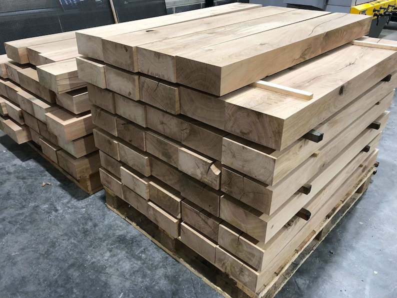 May include: A stack of wooden planks, likely for woodworking projects, are stacked on a pallet. The planks are light brown in color and have a rough texture.