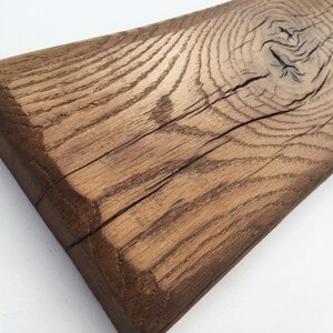 May include: A close-up of a rustic wooden plank with a natural brown finish. The wood has a knot and a crack running through it, showcasing its unique character.