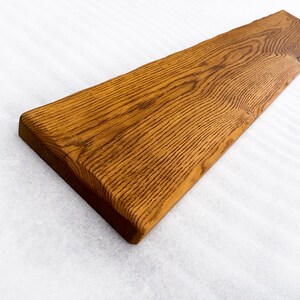 May include: A long, rectangular piece of wood with a natural, brown finish. The wood has a rough, textured surface and is slightly curved on one side.
