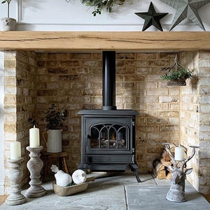 May include: A black cast iron wood-burning stove with a glass door and a brick fireplace surround. The fireplace has a wooden mantel and a decorative deer head candle holder.