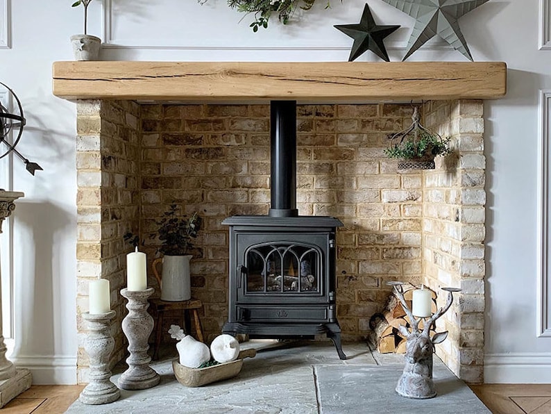 May include: A black cast iron wood-burning stove with a glass door and a brick fireplace surround. The fireplace has a wooden mantel and a decorative deer head candle holder.