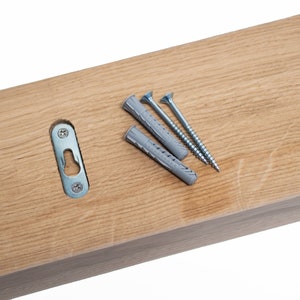 May include: A wooden shelf with a metal hanging bracket and three screws and plastic anchors. The shelf is light brown and the screws are silver.