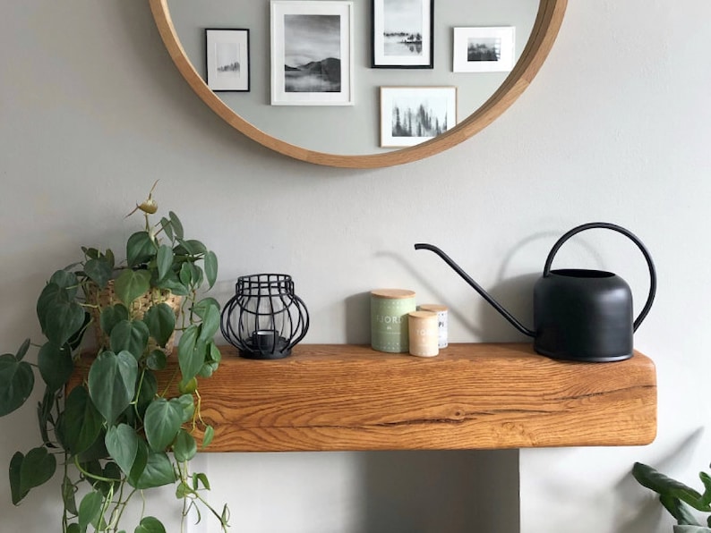 May include: A wooden shelf with a black watering can, three small jars, and a black metal candle holder. A potted plant with green leaves hangs over the shelf.