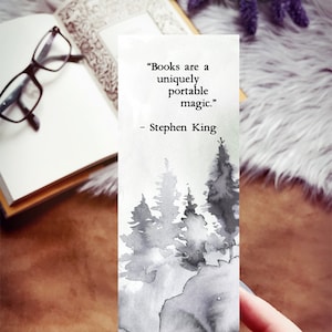 Puede incluir: Un marcap&aacute;ginas de acuarela en blanco y negro con una cita de Stephen King: "Los libros son una magia port&aacute;til &uacute;nica." La cita est&aacute; impresa sobre un fondo blanco con una ilustraci&oacute;n de acuarela de un bosque.