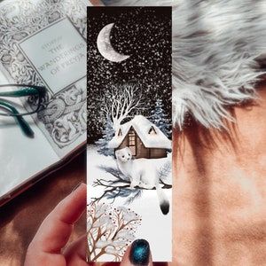 May include: A wintery bookmark featuring a small white house with a snowy roof and a white weasel standing on a branch. The background is a dark blue sky with falling snow and a crescent moon.