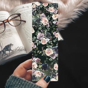 May include: A floral bookmark with a dark background and pink, purple, and white flowers. The bookmark is made of paper and has a matte finish.
