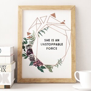 Può includere: Una stampa incorniciata con un design geometrico in oro e una ghirlanda di fiori. Il testo "She is an unstoppable force" è stampato in nero.