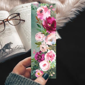May include: A watercolor bookmark featuring a vertical arrangement of pink, white, and burgundy flowers with green leaves on a green background.