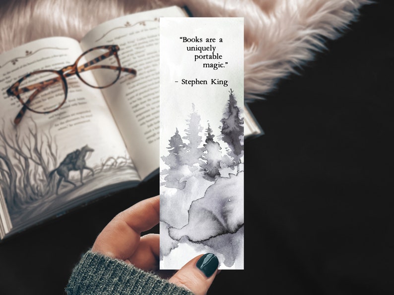 Puede incluir: Un marcap&aacute;ginas de acuarela en blanco y negro con una cita de Stephen King: "Los libros son una magia port&aacute;til &uacute;nica." El marcap&aacute;ginas presenta una ilustraci&oacute;n de acuarela de un bosque con &aacute;rboles y niebla.